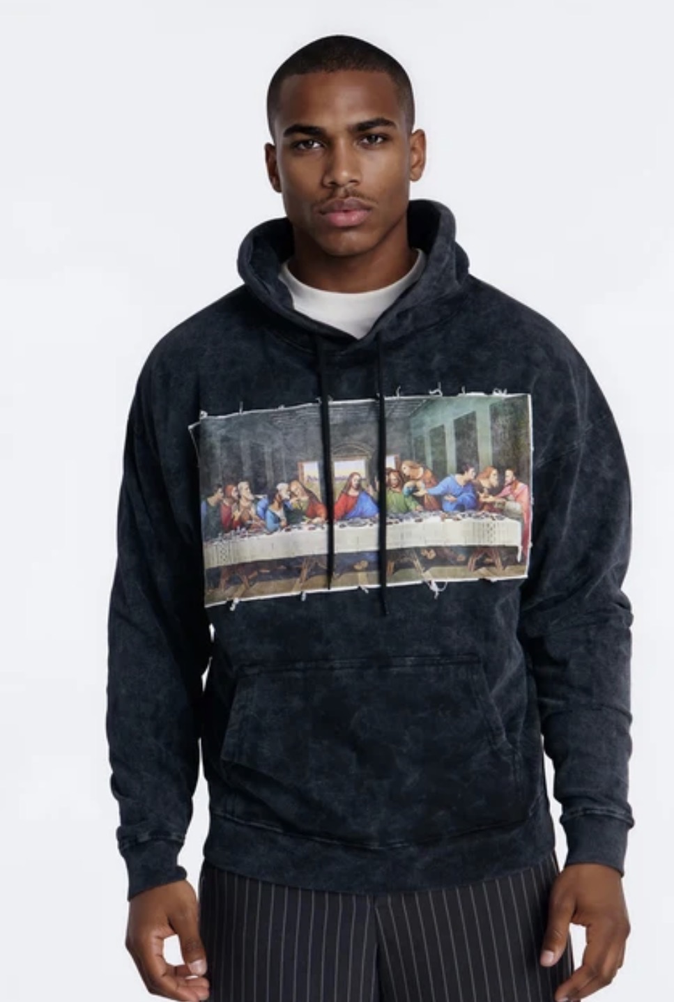 Model wearing a washed black hoodie with a raw-edge frayed patch of Da Vinci's The Last Supper